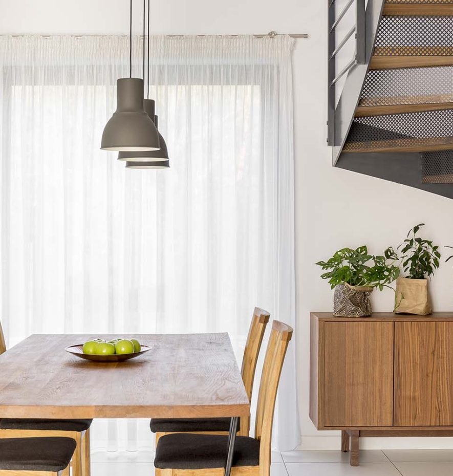 Dining room featuring a wooden table with green apples, modern pendant lighting, and a staircase, showcasing Rizo Homes' commitment to quality residential design.