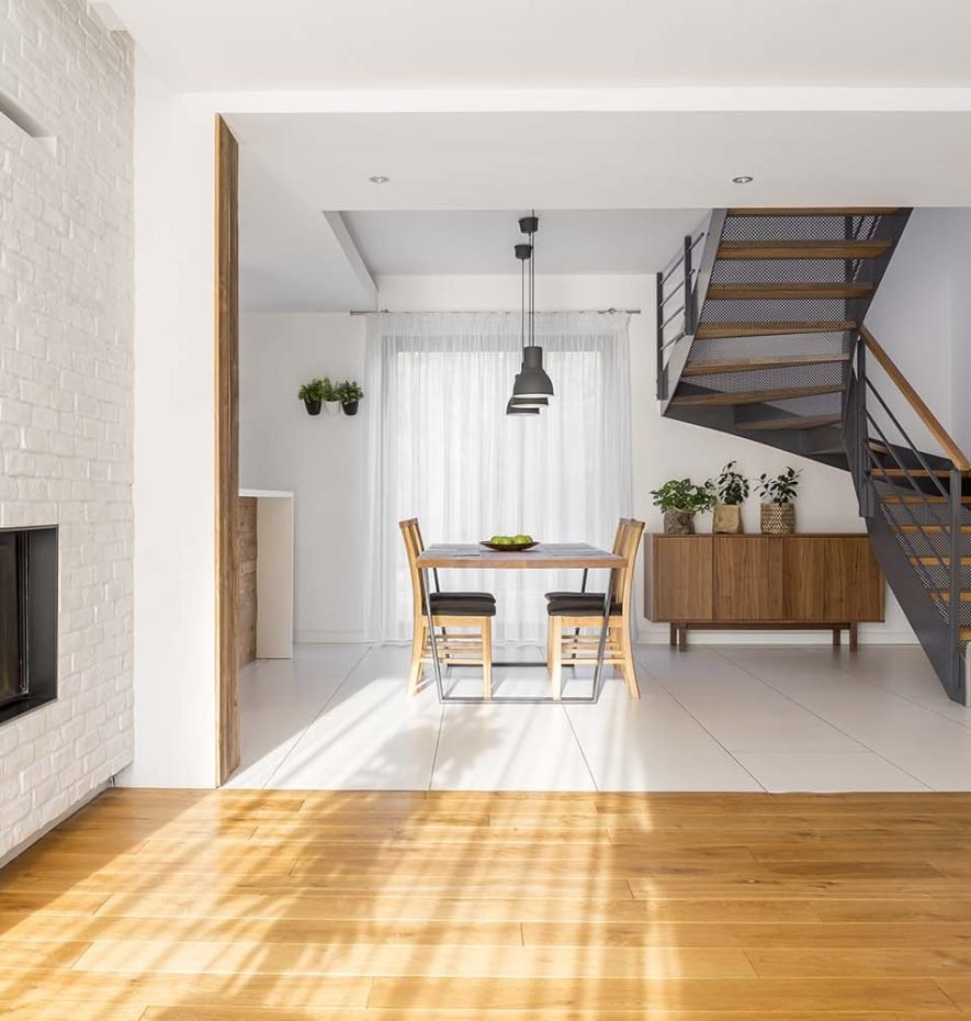 Modern dining area with a wooden table and chairs, contemporary staircase, large window with sheer curtains, and stylish decor, showcasing Rizo Homes' commitment to quality residential design.