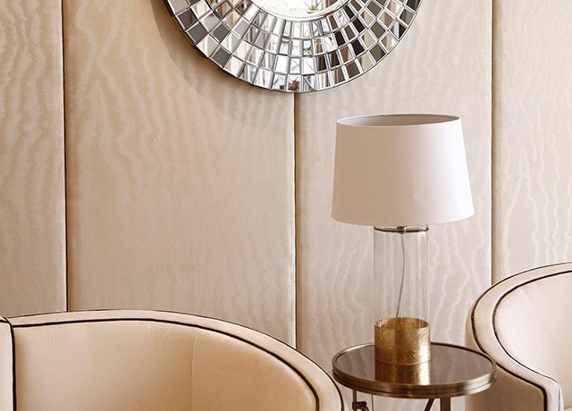 Elegant living room corner featuring plush cream chairs, a stylish round mirror, and a modern lamp on a gold side table, highlighting luxury interior design elements.