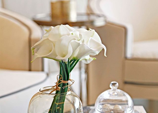 Elegant arrangement of white calla lilies in a glass vase, complementing a modern living space with neutral tones and stylish decor.