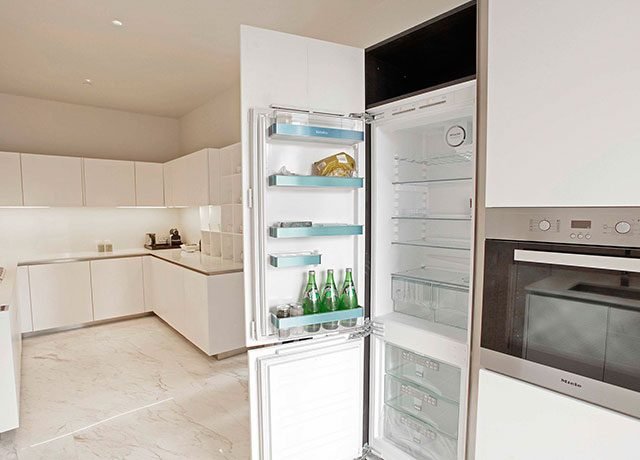 Modern kitchen featuring sleek white cabinetry, quartz countertops, and an open refrigerator displaying beverages, emphasizing luxury living and chef-ready design.